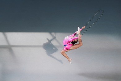 side view of female gymnast in pink dress with jumping rope. silhouette shadow on floor