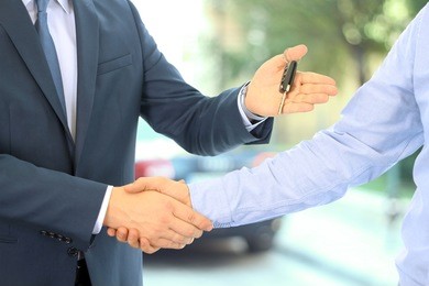 car salesman handing over the keys for a new car to a young businessman . handshake between two business people. focus on a key