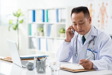 doctor checking his daily planner when talking to his patient on the phone
