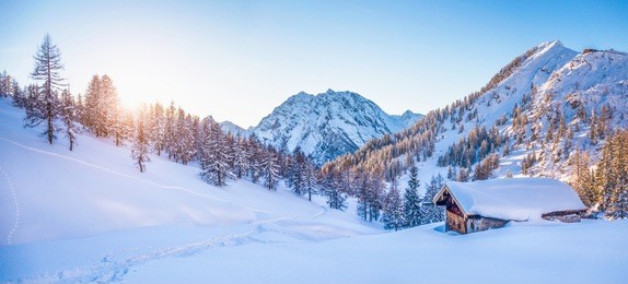 panoramic view of beautiful winter wonderland mountain scenery with traditional mountain cabin the background in the alps in golden evening light at sunset