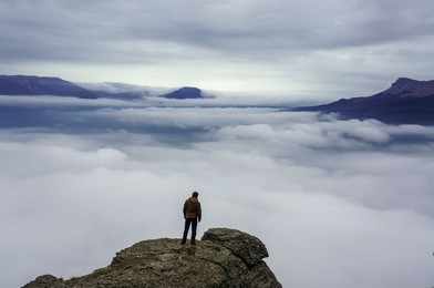 man standing on rock's edge above the clouds
