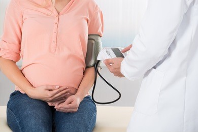 midsection of male doctor checking pregnant woman's blood pressure in hospital