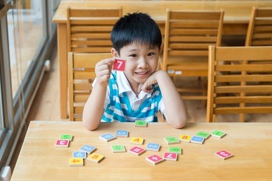 asian boy with wooden toy plate numbers on wood table ,he show  plate numbers in his hand