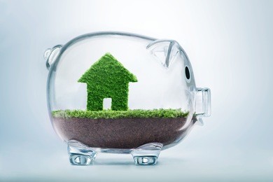 saving to buy a house or home savings concept with grass growing in shape of house inside transparent piggy bank