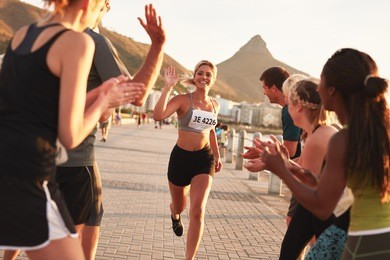 group of spectators cheering runners just before the finish line. female runner finishing the race with her team applauding her efforts.