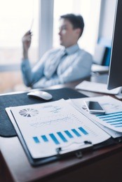 business documents on office table with smart phone and man working in the background