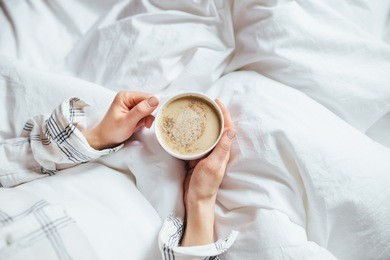 a cup of coffee in their hands in bed on a white blanket, simple, home, space in the frame