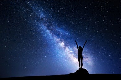 landscape with milky way. night sky with stars and silhouette of a standing girl with raised-up arms on the stone