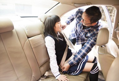 father securing daughter in the car seat