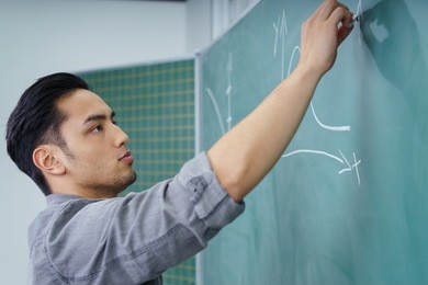 young asian male student writing on a chalkboard drawing graphs with a serious expression, close up profile view of his face