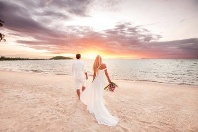 beautiful couple at sunset near the ocean.honeymoon romantic couple in love holding hands walking on beautiful sunset at beach. lovers or newlywed married young couple by the sea. wedding in thailand.