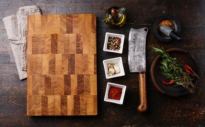 chopping cutting kitchen board, seasoning, herbs and butcher meat cleaver on dark wooden background