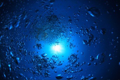 underwater view deep down with air bubbles and sun in the open ocean