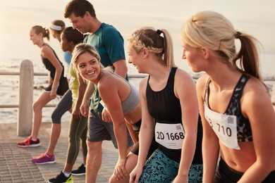 happy young woman standing at starting line along with competitors. racers standing at starting line of a marathon race.
