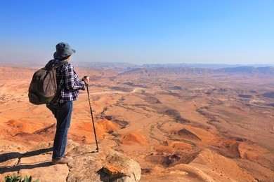 panoramic view of color stone desert of negev and traveler on the mountain top. national geological park hamakhtesh hagadol - large crater - a geological erosion land form, israel