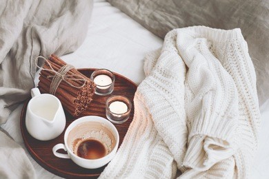 wooden tray with coffee, milk, cinnamon sticks and tea candles in the bed, lazy morning, warm winter mood