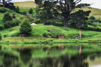hobbit holes in hobbiton movie set reflecting in a small lake. taken in new zealand.