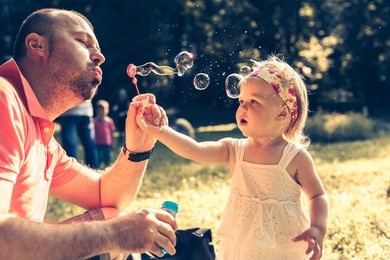 daddy and daughter blowing a bubbles in the park