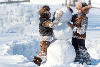 two little boys sculpt a snowman in the backyard of the house clear winter day