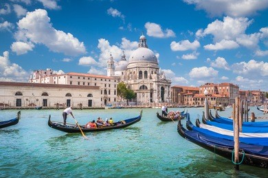 beautiful view of traditional gondolas on canal grande with historic basilica di santa maria della salute in the background on a sunny day with blue sky and clouds in venice, italy