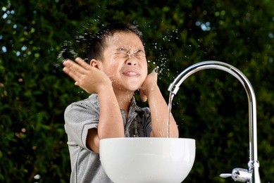 young asian boy washing his face by water from the brand new faucet.