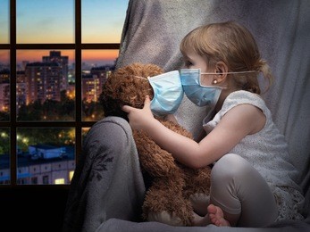 a child and a toy in a medical mask. the girl kisses a bear through the mask. house, evening, outside the city. conceptually about diseases, infection and allergy