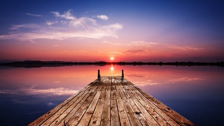 perspective view of a wooden pier on the pond at sunset with perfectly specular reflection