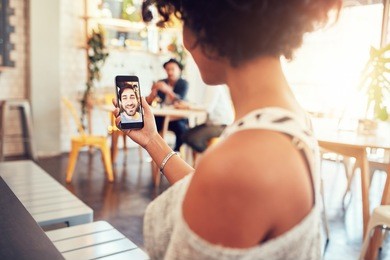 man and woman talking to each other through a video call on a smartphone. young woman having a videochat with man on mobile phone. woman sitting at a cafe.