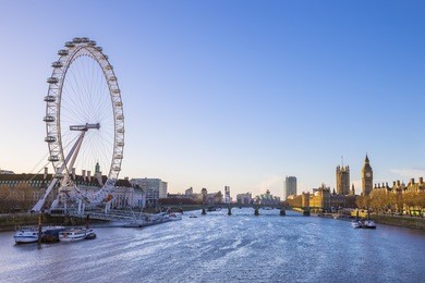 london skyline view at sunrise with famous landmarks, big ben, houses of parliament and ships on river thames with clear blue sky - england, uk