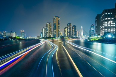 tokyo skyline by night in modern tsukishima district with scenic water reflection and boat light trail in sumida river waters. soft focus and motion blur due to long exposure shot.