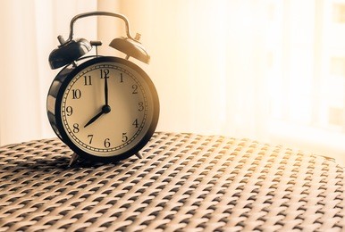 still life , vintage alarm clock on weave table with sunlight ( alarm clock show 8 o`clock )