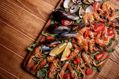 fresh mussels, crayfish, shrimp decorated with arugula, tomatoes, lemon and sauce on a wooden board. seafood platter