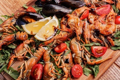 fresh mussels, crayfish, shrimp decorated with arugula, tomatoes, lemon and sauce on a wooden board. seafood platter