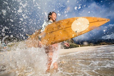 a surfing girl on a beach ready to go into the water. sunset time postcard style with warm tone and colors