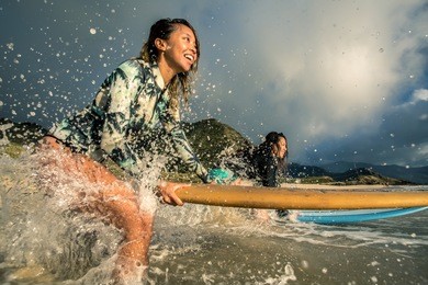 two surfing girls on a beach smiling and ready to go into the water.
