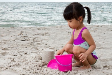 asian little chinese girl playing sand with beach toys on tropical beach