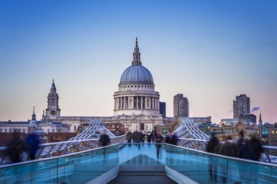 londoners walking through millennium bridge with st.paul's cathedral at the background after sunset - london, uk