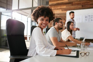 portrait of happy young african woman sitting at a business presentation with colleagues in boardroom. female designer with coworkers in conference room.