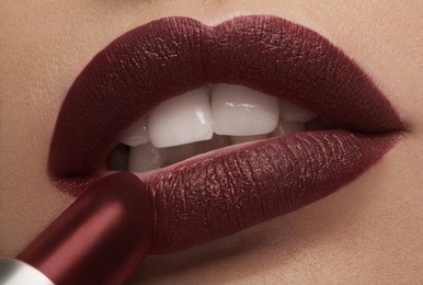 applying red lipstick on lips in close up photo in studio lighting