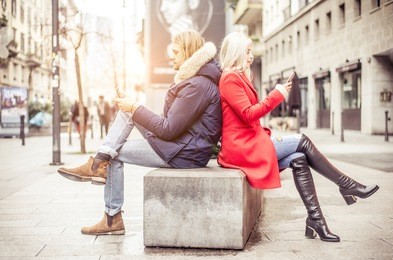 couple looking at cellphones and showing mutual disinterest - man and woman writing sms on smartphones
