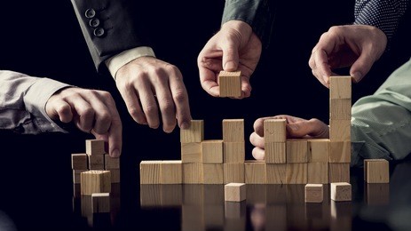 teamwork and cooperation concept - five male hands building a structure of wooden blocks on black desk with reflection, toned retro effect.