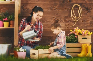 cute child girl helps her mother to care for plants. mother and her daughter engaged in gardening in the backyard. spring concept, nature and care.