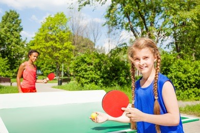 two happy girls playing ping pong outside during summer sunny day