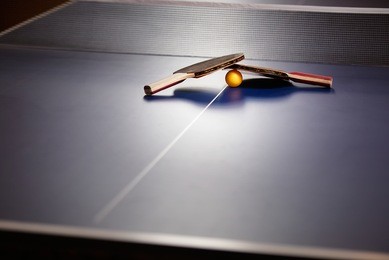 two table tennis or ping pong rackets and ball on a blue table with net