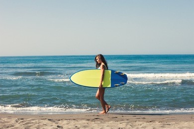 young woman prepare for surf on board full body shot on sandy beach by the sea