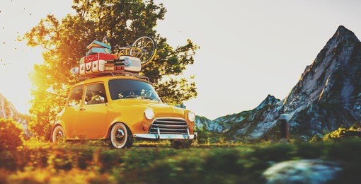 cute little retro car with suitcases and bicycle on top goes by wonderful countryside road at sunset