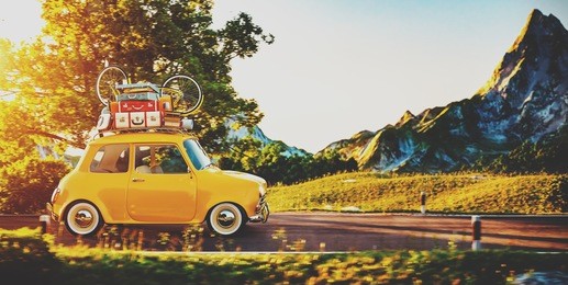 cute little retro car with suitcases and bicycle on top goes by wonderful countryside road at sunset
