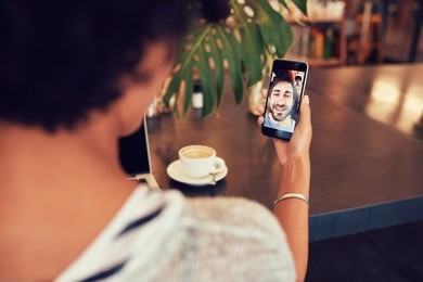 young an and woman talking to each other through a video call on a smartphone. young woman having a videochat with man on mobile phone. woman sitting at a coffee shop.