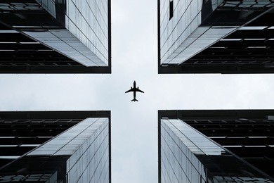 silhouette of an airplane flying into the crosshair of a symmetrical highrise building.
