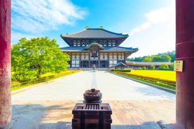 incense burner and pillars in foreground leading to front facade of the great buddha hall daibutsuden at todai-ji temple on a beautiful blue sky morning with nobody present in nara, japan. horizontal